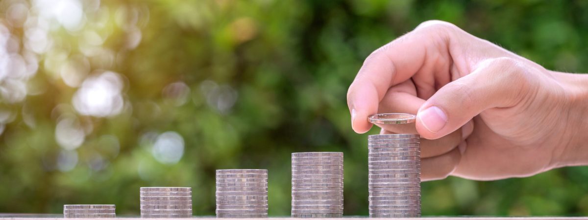 Hand holding coin and stack of money on wood table. Pension fund concept.